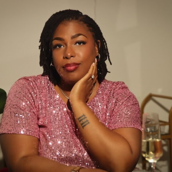 LAUNA in a pink sequin top resting her chin on her hand, smiling softly