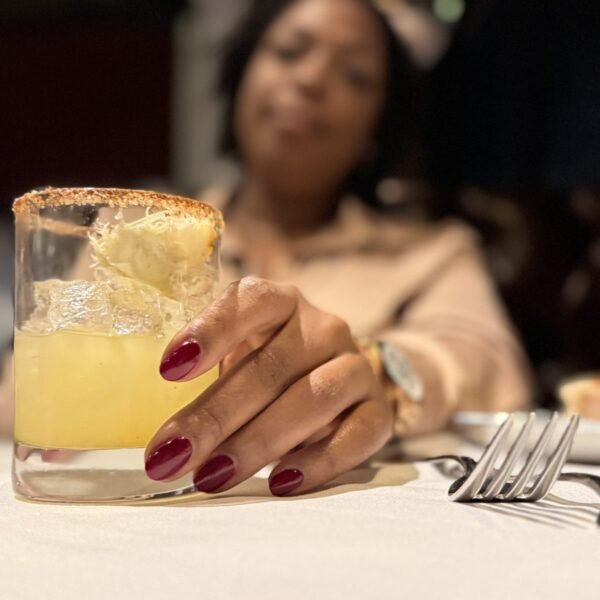 A cocktail on a linen-covered table, Launa's manicured hand resting on the glass