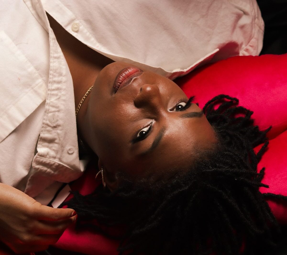 Launa reclining against a cream and pink backdrop in a linen shirt