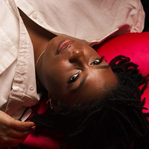 Launa reclining against a cream and pink backdrop in a linen shirt