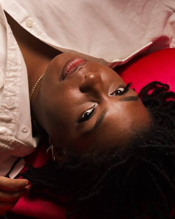 Launa reclining against a cream and pink backdrop in a linen shirt